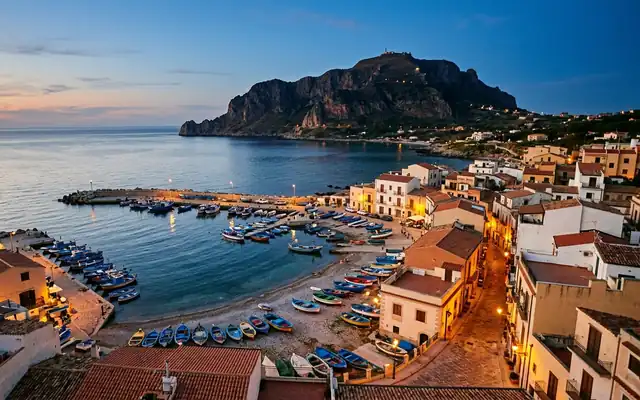 Aspra at dusk, colorful fishing boats pulled up along the harbour on the Gulf of Palermo with a rocky headland behind
