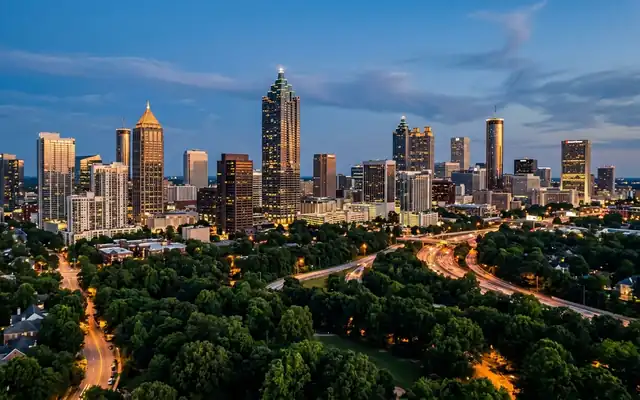 The Atlanta skyline with the spire-topped Bank of America Plaza above a canopy of trees at dusk