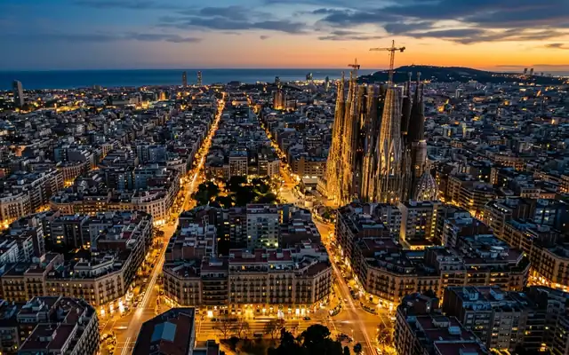 The Sagrada Familia towers above Barcelona's Eixample grid with the sea beyond at dusk