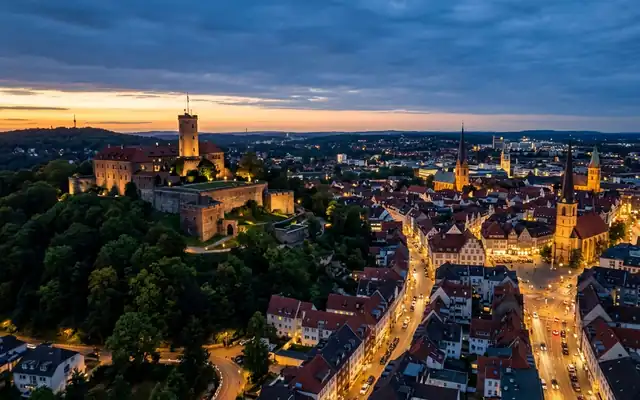 Bielefeld at dusk, the hilltop Sparrenburg castle and its round tower above the wooded slope and lit old town streets