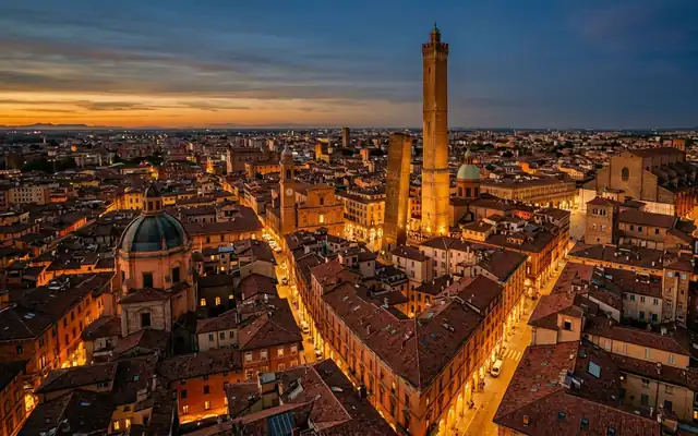 The Two Towers rising above Bologna's terracotta rooftops and lit streets at dusk