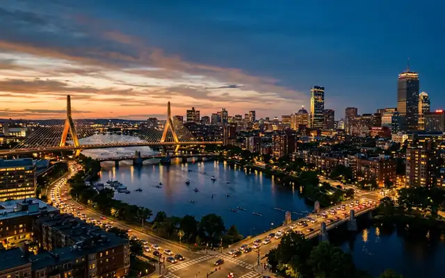 The Zakim Bridge and Boston skyline across the Charles River with rowers on the water at dusk
