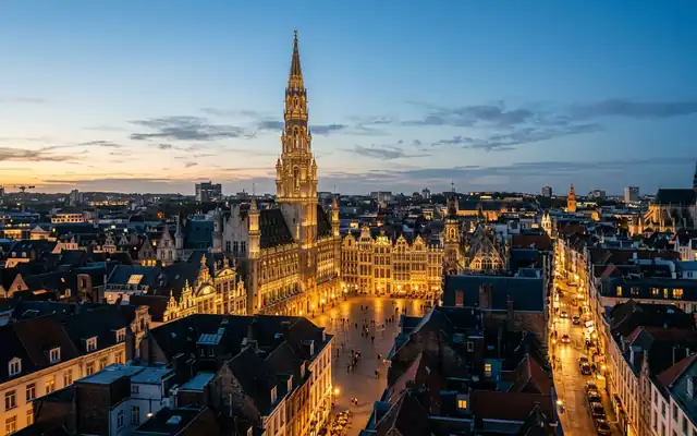 The illuminated Gothic town hall tower above Brussels' Grand Place and old town rooftops at dusk