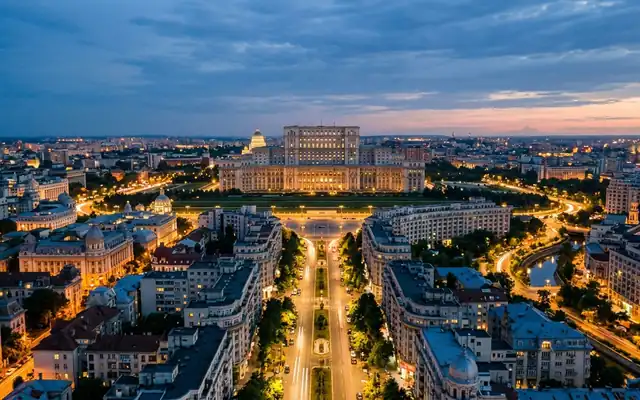Bucharest at dusk, the Palace of the Parliament at the head of a wide boulevard lined with symmetrical apartment blocks