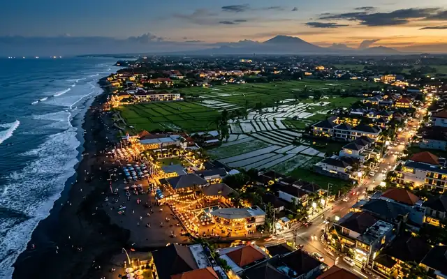 Canggu at dusk, the black sand beach at Batu Bolong lined with lit beach clubs and rice paddies inland