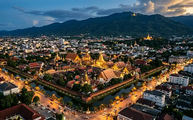 Aerial view of Chiang Mai's moated Old City with golden temple rooftops and Doi Suthep mountain at dusk