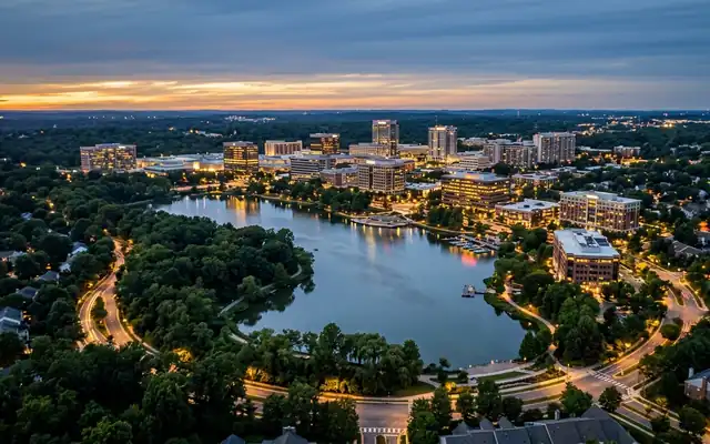 Columbia at dusk, the wooded shores of Lake Kittamaqundi with downtown's low office towers and a lit lakefront promenade