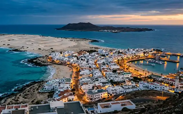 The white houses and harbour of Corralejo with sand dunes and Lobos Island offshore at dusk