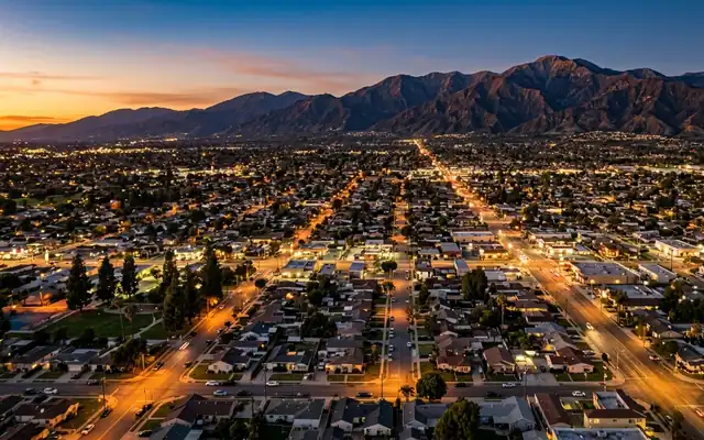 Covina at dusk, a low rise suburban grid of lit streets with the San Gabriel Mountains on the horizon