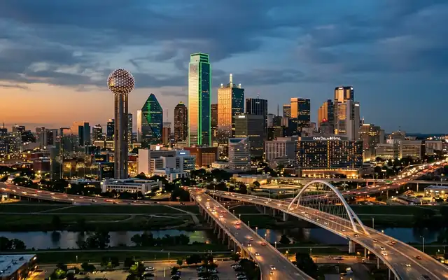 Reunion Tower's lit sphere beside the downtown Dallas skyline and freeways at dusk