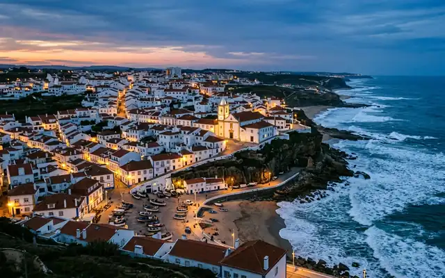 Ericeira at dusk, whitewashed red roofed houses on the clifftop above fishing boats and Atlantic surf