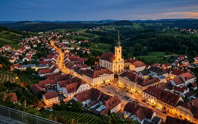 Gleisdorf at dusk, red tiled rooftops around the parish church spire and main square amid the rolling hills of Styria
