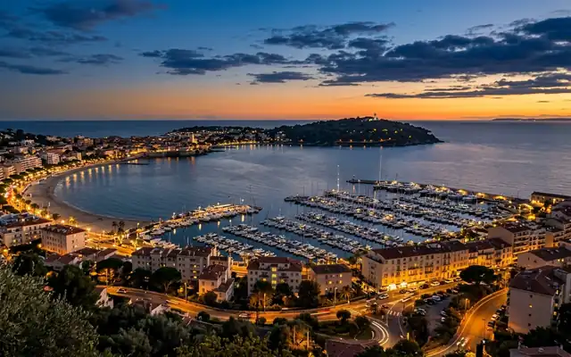 Golfe-Juan at dusk, yachts filling the marina beside the curving bay beach with the wooded Cap d'Antibes headland across the water