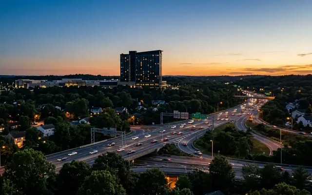 Hanover at dusk, a hotel tower silhouetted above wooded suburbs with traffic on the highway interchange and a mall below