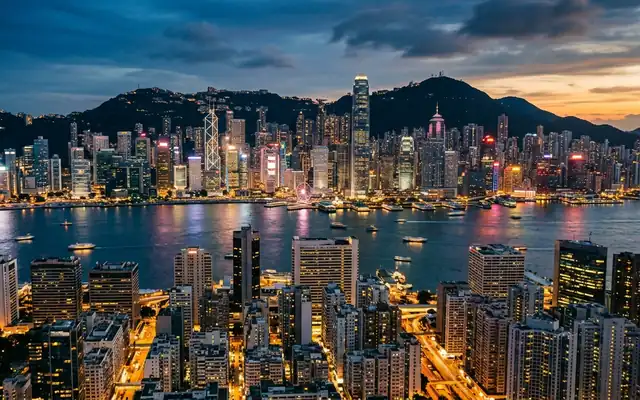 Hong Kong at dusk, the dense Victoria Harbour skyline with the Bank of China Tower below the ridge of Victoria Peak