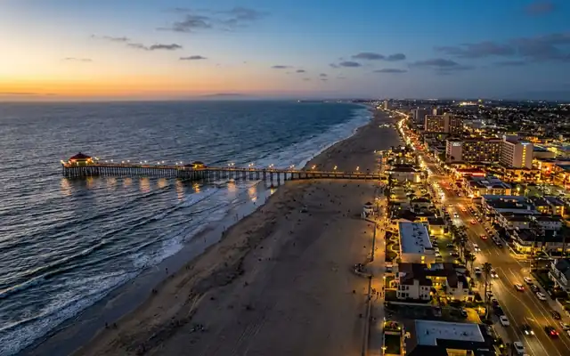 Huntington Beach at dusk, the long pier reaching into Pacific surf beside the wide sandy beach and lit coastal strip