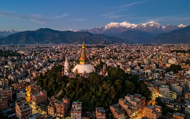 Kathmandu in the evening, the hilltop Swayambhunath stupa with its gilded spire above dense valley rooftops and Himalayan ridges