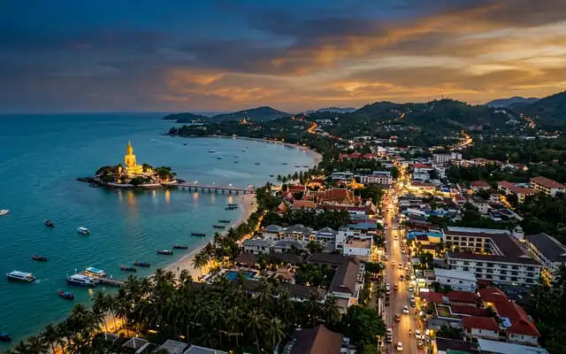 The golden Big Buddha on its islet off Koh Samui with beaches and village lights at dusk