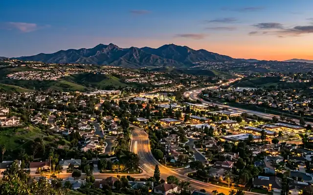 Laguna Hills at dusk, suburban homes across rolling green hills with the Saddleback Mountain ridge dark on the horizon