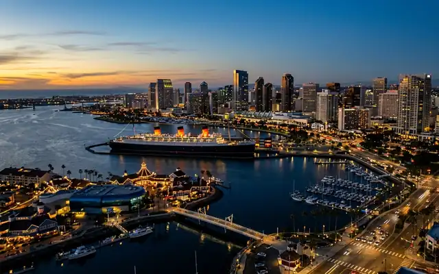 Long Beach harbor at dusk, the Queen Mary ocean liner moored across the water from the downtown skyline