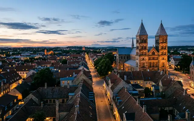 Lund at dusk, the twin-towered Romanesque Lund Cathedral lit above the old town rooftops and a straight lamplit street