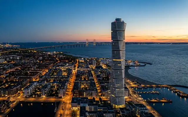 The twisting Turning Torso tower over Malmo's waterfront with the Oresund Bridge in the distance at dusk