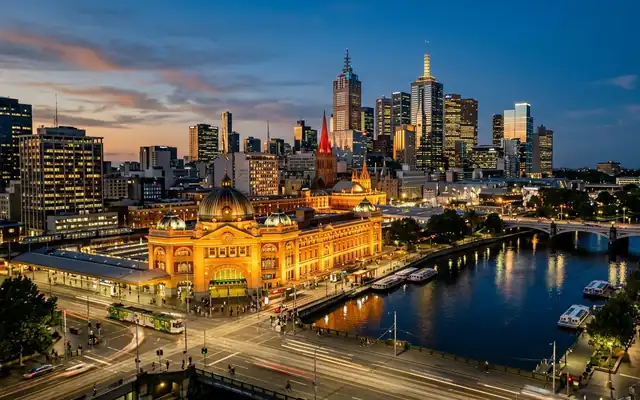Flinders Street Station's yellow facade and dome with Melbourne's skyline and the Yarra River at dusk