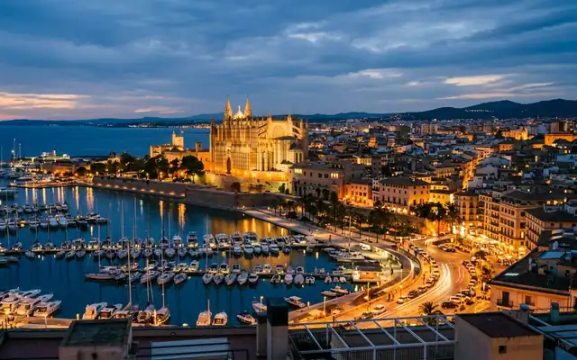 The illuminated Gothic cathedral of Palma de Mallorca above the seafront marina and bay at dusk
