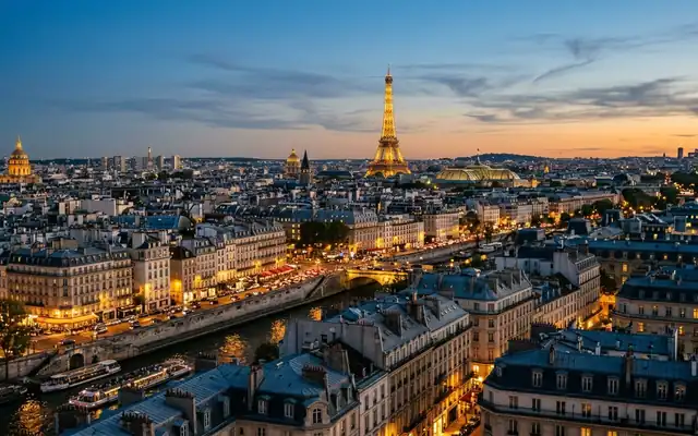 The illuminated Eiffel Tower above Haussmann rooftops and the Seine in Paris at dusk