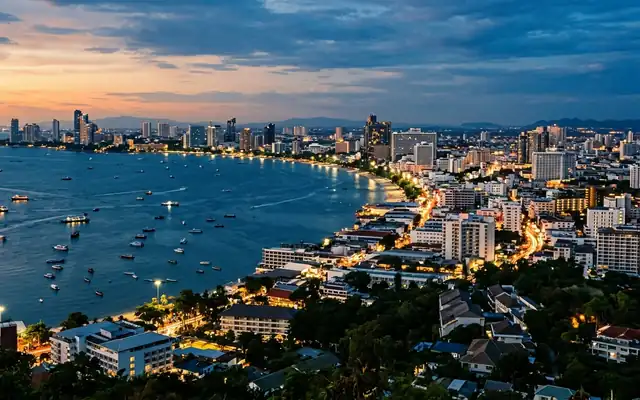 The curving bay of Pattaya lined with lit beachfront high-rises and boats at dusk