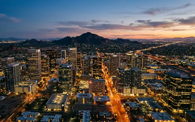 Downtown Phoenix skyline lit at dusk, low-rise towers spread across the desert valley with a dark mountain on the horizon