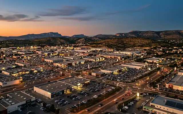 Plan de Campagne retail park at dusk, rows of low commercial buildings and car parks below dry Provencal hills