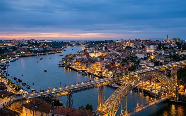 Porto at dusk, the double-deck iron arch of the Dom Luis I Bridge over the Douro beside the terraced Ribeira
