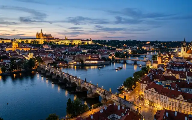 Prague Castle above the Vltava river with the Charles Bridge and red rooftops at dusk