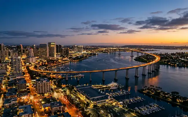 The curving Coronado Bridge spanning San Diego Bay beside the downtown skyline at dusk