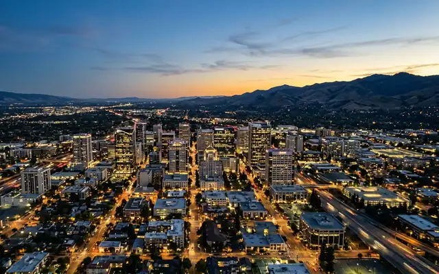 Downtown San Jose at dusk, its high-rise cluster across the flat Santa Clara Valley with mountain ranges on both horizons