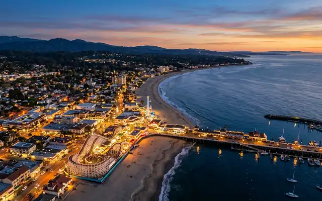 Santa Cruz at dusk, the Beach Boardwalk with its wooden Giant Dipper coaster and the wharf along curving Monterey Bay