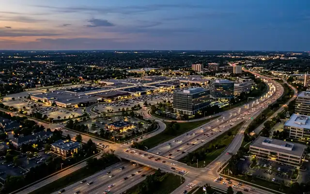 Schaumburg at dusk, the Woodfield Mall complex and glass office buildings along the tollway with traffic on the lanes below