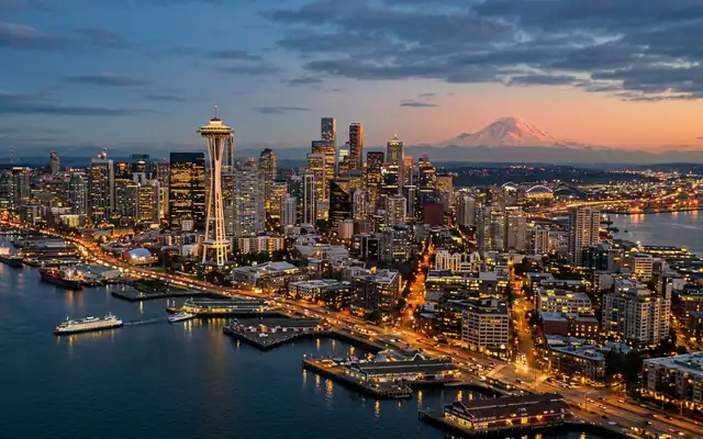 The Space Needle and Seattle skyline over Elliott Bay with Mount Rainier on the horizon at dusk