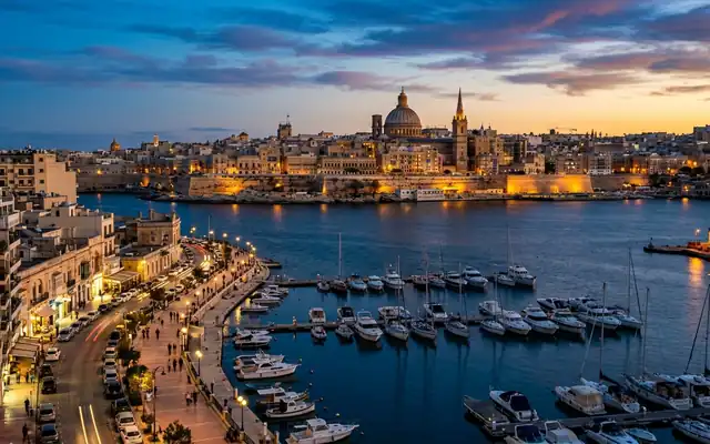 Valletta's domed skyline across the harbour from Sliema's boat-lined waterfront at dusk