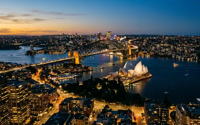 The Sydney Opera House and Harbour Bridge across the harbour water at dusk