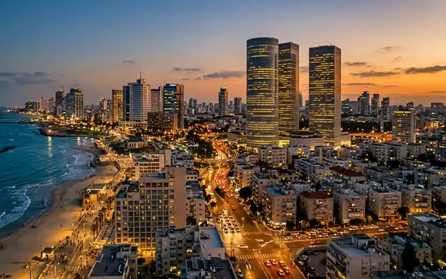 Tel Aviv's beachfront and dense skyline with three lit towers above busy streets at dusk