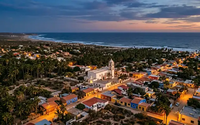 Todos Santos at dusk, the white mission church and low colourful houses among palm groves with the Pacific Ocean beyond