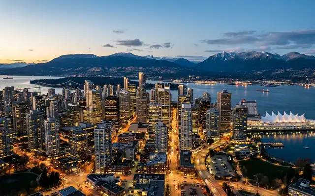 Vancouver at dusk, the glass downtown towers on Burrard Inlet with Canada Place and the snow-capped North Shore mountains behind