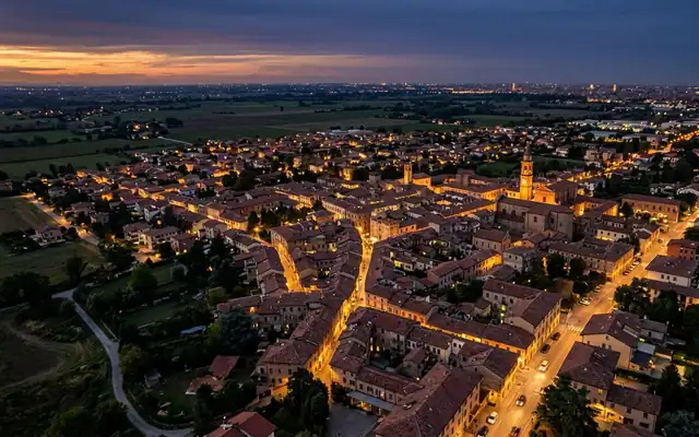 Villanova di Castenaso at dusk, red-tiled rooftops and a church bell tower amid the flat fields of the Emilian plain