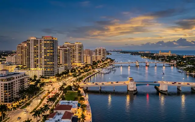 West Palm Beach at dusk, downtown towers and palm-lined shore with two bridges crossing the Intracoastal Waterway to Palm Beach