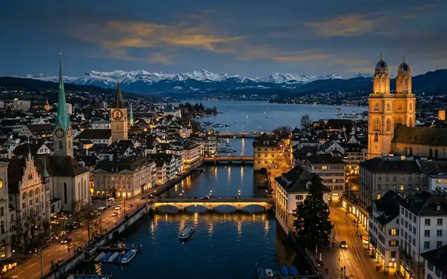Zurich old town and the Grossmunster towers on the Limmat, with the lake and snowy Alps at dusk