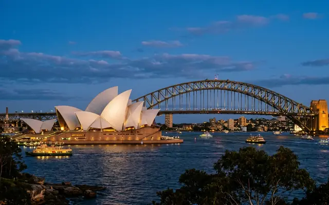 Sydney Harbour at dusk in Australia, the white sail shells of the Opera House with the Harbour Bridge arch behind