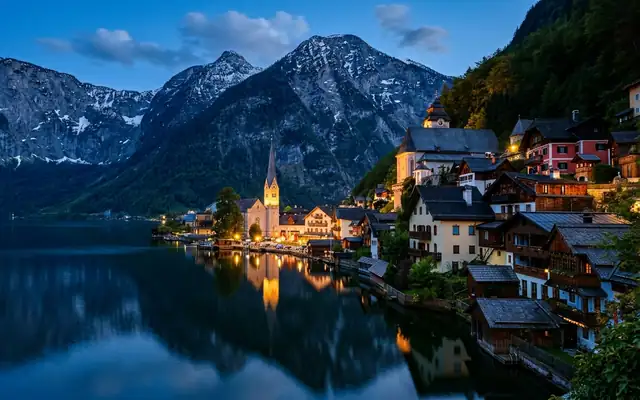 Hallstatt at dusk beside the lake in Austria, the church spire and pastel houses below steep snow-streaked Alpine peaks