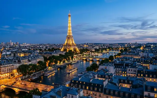 The Eiffel Tower lit above Paris rooftops and the Seine at dusk in France, bridges and river boats below